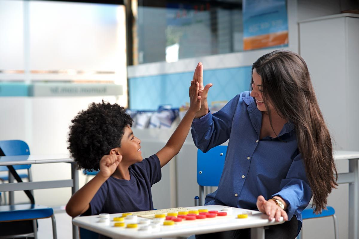 Orientadora do Kumon realizando o gesto de high five com o aluno que fez toda a lição
